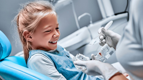 Smiling young girl in dental chair learning about teeth with dentist 