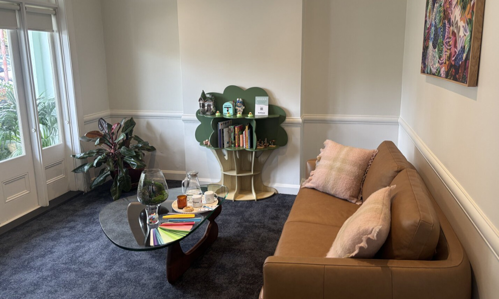 Cozy dental waiting area with leather sofa, tree-shaped bookshelf, glass coffee table, and natural light